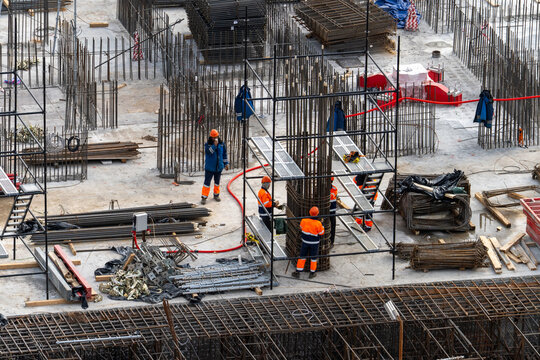 Builders in overalls at a construction site, top view. Workers erect iron and concrete monolithic structures during the construction of a building