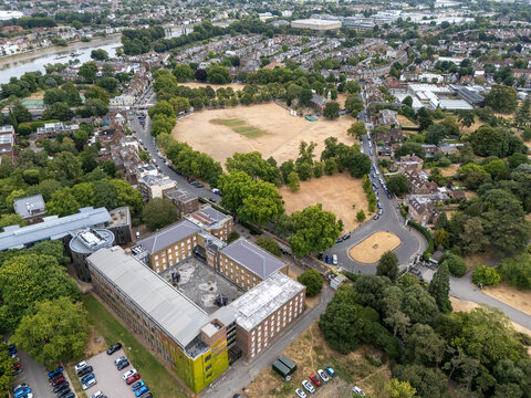Aerial view of the Herbarium and Library building complex surrounded by lush trees, a large open field, and urban infrastructure in Richmond, England, United Kingdom.