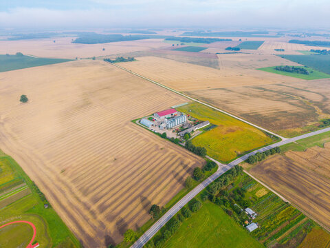 Aerial view of a farm with grain silos surrounded by harvested agricultural fields and a road in Jaunberze Parish, Dobele Municipality, Latvia.