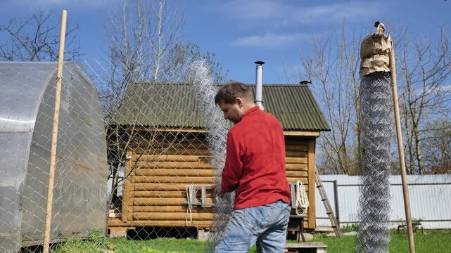 A man is unrolling a roll of wire mesh fencing.