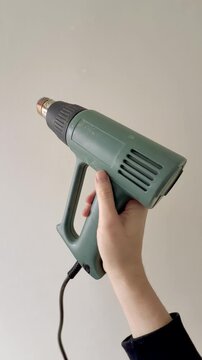 Hand Holding Green Heat Gun Against Plain Wall Vertical
