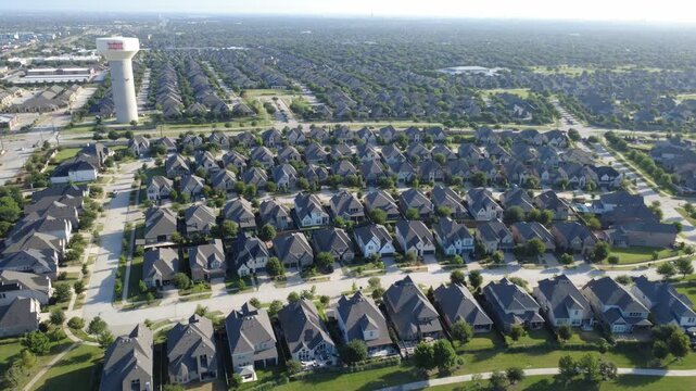 Densely arranged residential streets border green parkways near Phillips Creek Ranch. Aerial perspective showcases uniform rooflines, neighborhood lawns, civic utility structure, Frisco, TX