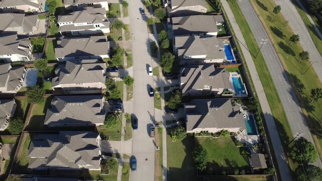 Concrete cul de sac divides two rows of upscale suburban single-family homes in Dallas Fort Worth metroplex. Top-down aerial shows parked vehicles, private pools, boulevard lawns in Frisco, Texas