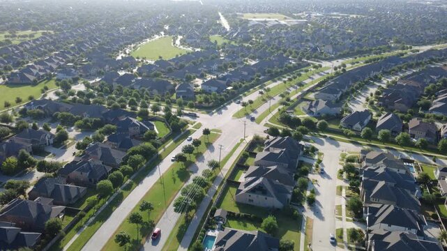 Suburban thoroughfares cross near brick residential blocks in Denton County. High angle view reveals backyard swimming pools, paved neighborhood streets, green greenways in Frisco, Texas