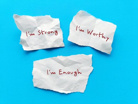 Three paper notes on blue background with handwritten text I AM STRONG, I AM WORTHY, I AM ENOUGH - powerful self talk positive affirmations to boost self confidence in daily life