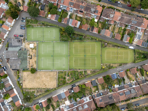 Aerial view of the tennis courts at Gunnersbury Triangle Sports Field surrounded by residential houses and gardens in London, England, United Kingdom.
