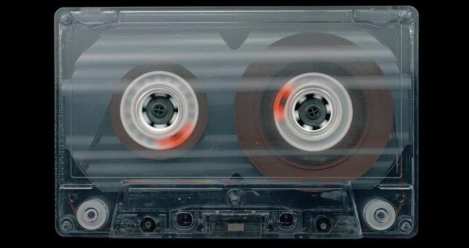 Audio Cassette Tape Winding. Transparent vintage cassette with spinning reels transferring magnetic tape on a black background.