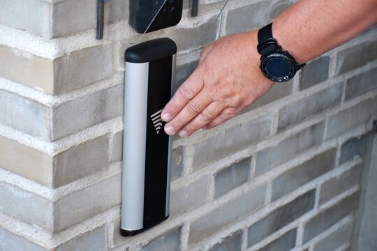 A man's hand presses an automatic door opener button on a brick wall. Using a push or proximity switch in an access control system to automatically open doors.