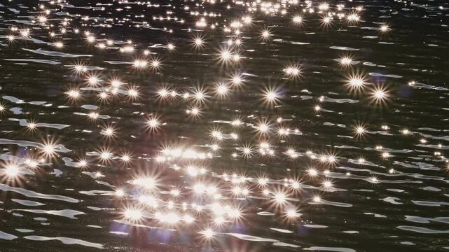 Bright sun glints sparkling on water surface. Beautiful starburst reflection of sun light on ripples of dark sea or river. Glittering natural background.