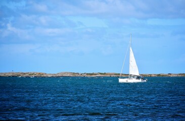 Fototapeta premium A white sailing yacht sails across the sea against a backdrop of a rocky coastline. Seascape.