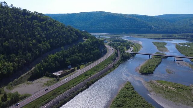Drone footage captures traffic on iconic Route 132 running beside the legendary Matapedia River and a railway through lush Appalachian mountains in Quebec.