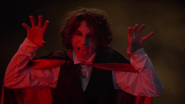Portrait of Caucasian teenager wearing vampire costume turning around, opening cape, and screaming at camera. Footage is ideal for Halloween marketing campaigns and seasonal retail promotions