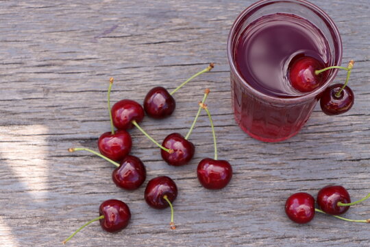 Top view of a glass of cherry drink and a handful of ripe cherries on a wooden board.