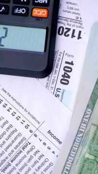 Calculating Income Tax Return. A hand enters figures on a calculator beside tax forms, dollar bills, and a pen.	
