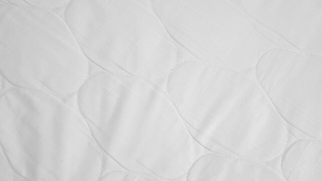 Panning across a white quilted mattress protector fabric. Concept of comfortable bedding, clean bedroom textiles, and soft sleeping materials.