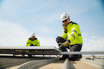 Fototapeta premium Solar panel technician worker roof safety helmet high visibility construction renewable energy installation maintenance on rooftop with two engineers using radio under blue sky