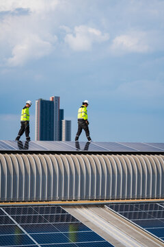 Solar panel worker roof safety helmet construction renewable energy city sky, worker in safety vest and helmet walking on rooftop solar panel above urban building under cloudy blue sky