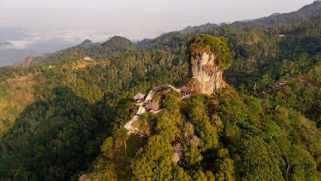Aerial view of Puncak Widosari rock formation surrounded by lush green hills and forest in Kecamatan Samigaluh, Daerah Istimewa Yogya, Indonesia.