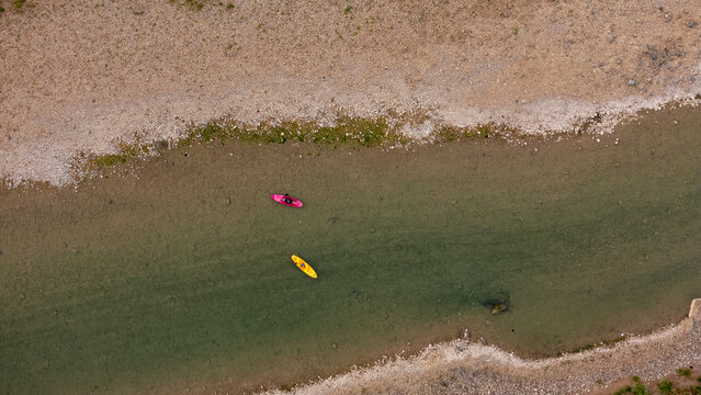 Aerial view of Sungai Oya with a pink kayak and a yellow kayak floating on the clear water near a gravel riverbank in Kecamatan Imogiri, Daerah Istimewa Yogya, Indonesia.