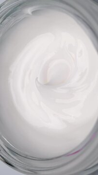 White Cream Swirling. Thick glossy cream moves in smooth folds, creating a soft abstract cosmetic texture.	