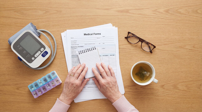 Senior hands reviewing medical forms beside blood pressure monitor pillbox tea, authentic active aging concept showing independence confidence value value value value value value value
