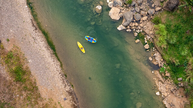 Aerial view of two kayaks paddling on Sungai Oya with rocky banks and lush vegetation in Kecamatan Imogiri, Daerah Istimewa Yogya, Indonesia.