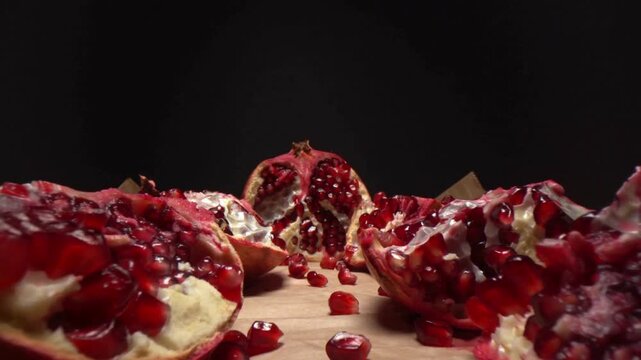 Vibrant ruby-red pomegranates, some artfully broken open to reveal a bounty of juicy arils, scattered on a rustic wooden surface against a moody backdrop, symbolizing freshness and healthy living