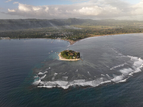 Aerial view of a small tropical island with lush vegetation and sandy beaches surrounded by coral reefs and deep blue ocean waters near the coast of Port Vila, Shefa Province, Vanuatu.