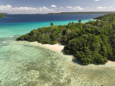 Aerial view of the lush tropical coastline with turquoise reef waters and white sand beach in Vava'u, Tonga.