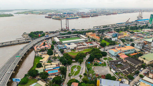 Aerial view of Lagos Island featuring the Onikan Stadium, the busy Carter Bridge spanning the lagoon, and the dense urban landscape with ships docked at the port in Lagos, Lagos, Nigeria.