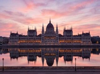 Naklejka premium Majestic sunset view of the illuminated Hungarian Parliament Building reflecting in the Danube River, Budapest
