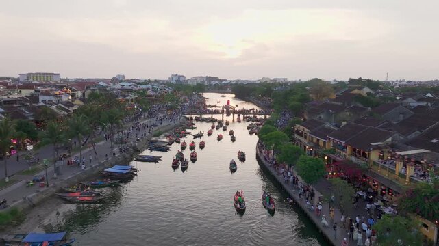 Drone flying over Thu Bon River and Hoi An Ancient Town at sunset with boats and lanterns, Vietnam