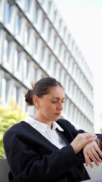 Businesswoman waiting on a bench near office buildings, looking around with concern, representing uncertainty, delayed meetings, business stress, and urban professional life.