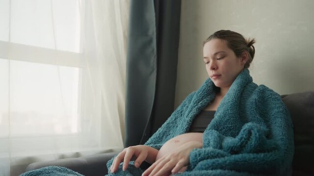 Pregnant white woman by window wrapped in teal blanket, soft morning light, gazing outside with gentle smile, connecting with unborn baby, nesting energy and prenatal calm, quiet anticipation