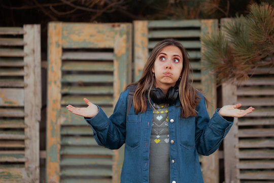 Confused Woman In Denim Jacket Shrugging in front of Closed Restaurant.  Puzzled female tourist wearing sweater and headphones looks back with a shrug inside deserted building
