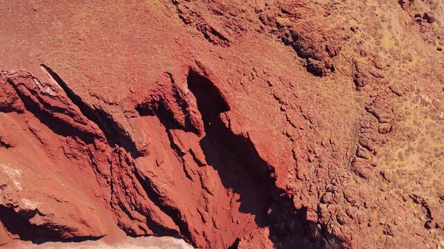 Drone view looking down at dramatic red volcanic cliffs and rock formations at Red Beach Santorini