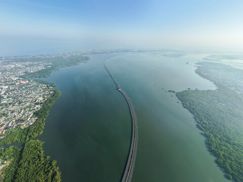 Aerial view of Mandara Toll Road stretching across the water, connecting coastal areas with lush mangroves and urban development in Kecamatan Kuta Selatan, Bali, Indonesia.
