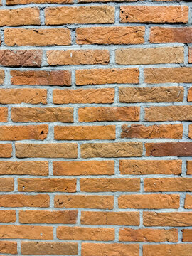 Close-up of a rustic orange brick wall with textured surfaces and gray mortar joints.
