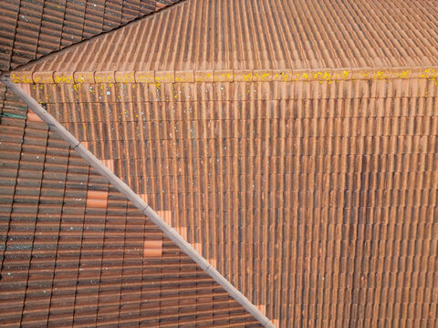Aerial view of brown clay roof tiles with patches of yellow lichen and geometric roof lines in Kempele, North Ostrobothnia, Finland.