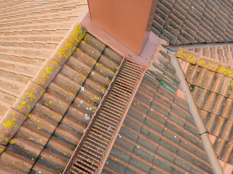 Aerial view of a tiled roof featuring yellow lichen growth, a metal chimney, and a roof ladder in Kempele, North Ostrobothnia, Finland.