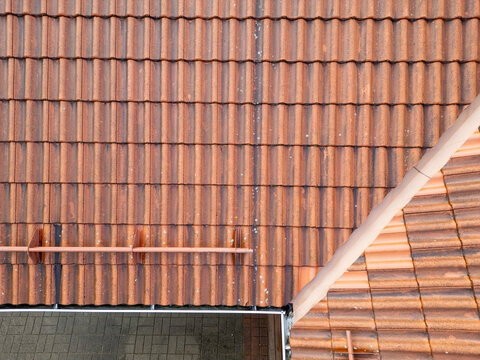 Aerial view of red clay roof tiles with patches of lichen, featuring a metal snow guard and gutter system in Kempele, North Ostrobothnia, Finland.