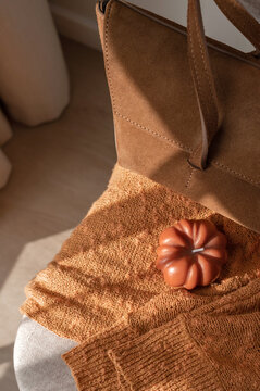 Fashion autumn aesthetic still life, terracotta knitted clothing on chair, caramel sueded bag, pumpkin candle with soft natural sunlight, lifestyle home interior