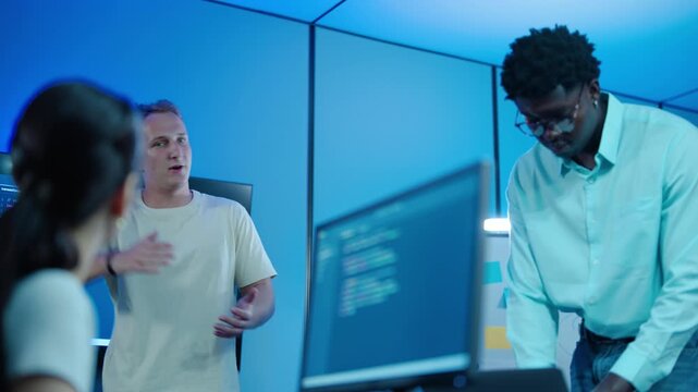 Diverse IT professionals discussing software code on large screens in a modern blue lit tech office. A team of programmers collaborating on a cybersecurity project during an important meeting.