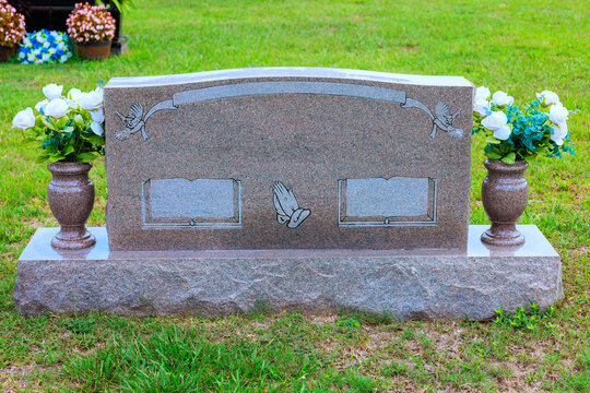 Gravestone with flowers on green lawn in cemetery during day