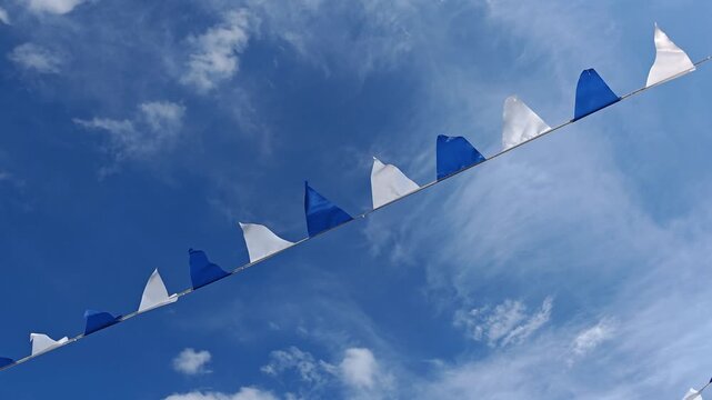 Blue and white bunting flags flutter against a bright cloudy sky, festive outdoor decoration, cheerful celebration, summer event, community gathering.