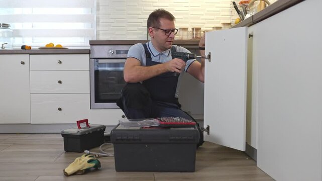 Handyman repairing a kitchen cabinet door hinge with a power drill