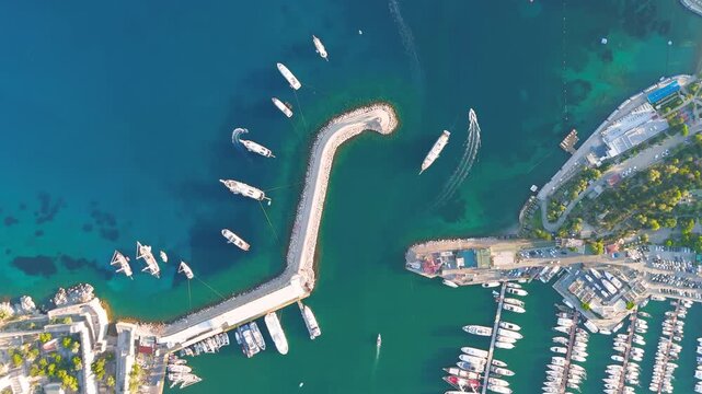 Bodrum, Turkey. Aerial top-down view of Bodrum Marina entrance, a sweeping stone breakwater guiding yachts and sailboats through turquoise Aegean waters. Aerial View, HEAD OVER SHOT