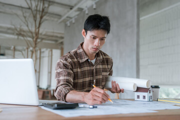 Fototapeta premium Architect working at a laptop with architectural blueprints in a modern studio, representing building design, construction planning, engineering, and professional project development.