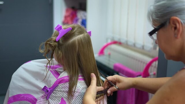 Hairdresser cutting long blonde hair of a little girl in a salon