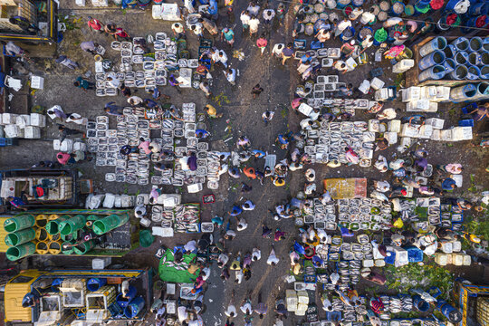 Aerial view of a busy fish market with vendors and buyers navigating between crates of fresh fish, colorful containers, and transport trucks in Chattogram, Chittagong Division, Bangladesh.